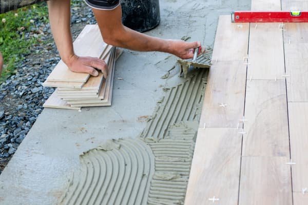 Handwerker verlegt Bodendielen im Dünnbettmörtel mit Zahnkelle